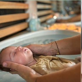 Un nouveau-né enveloppé dans un lange, porté dans l'eau par les mains d'une adulte lors d'un bain enveloppé.